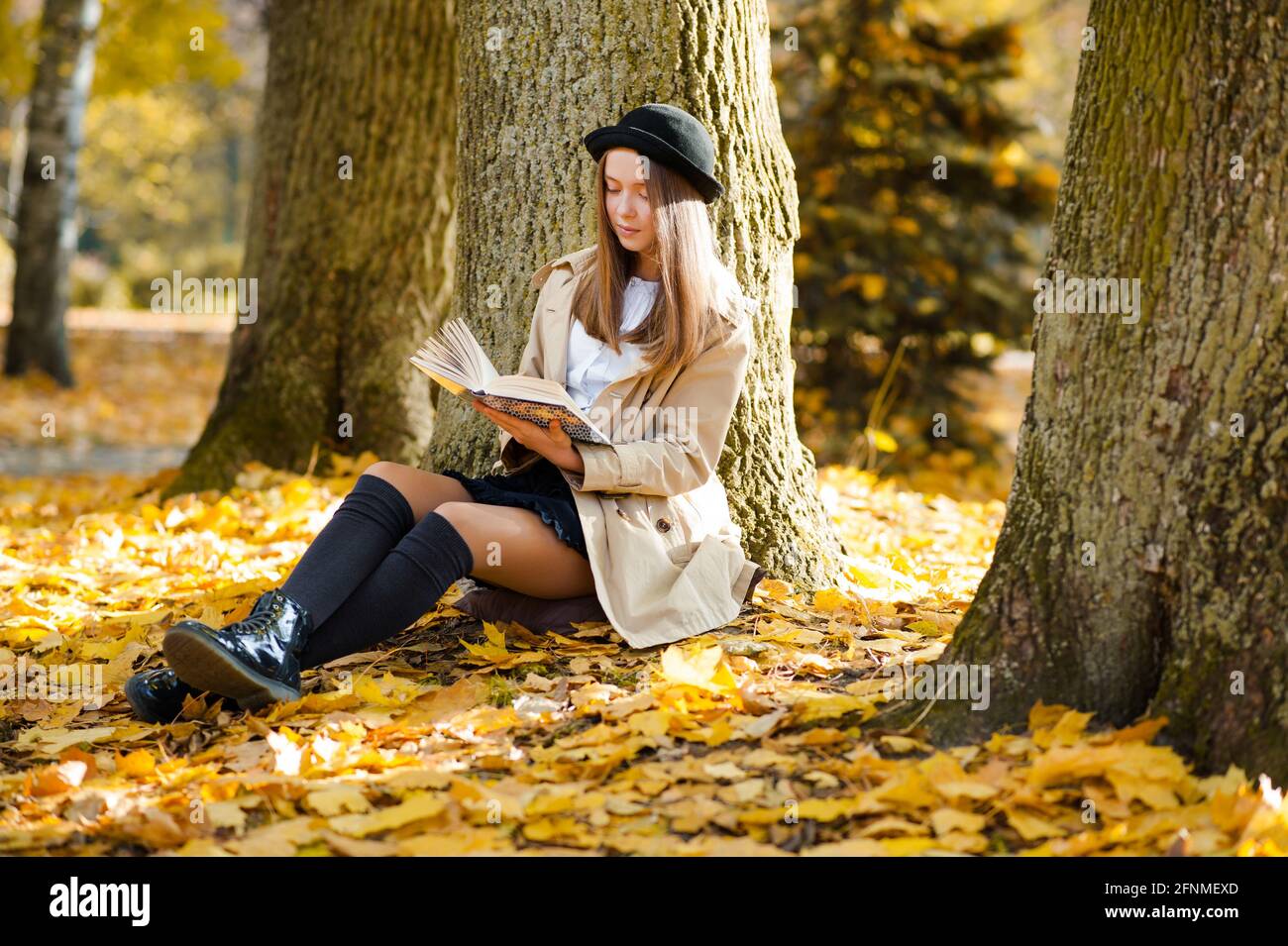 Ihr ruhiger Ort. Horizontales Porträt eines schönen jungen Mädchens, das ein Buch liest, das in der Nähe eines Baumes sitzt Stockfoto