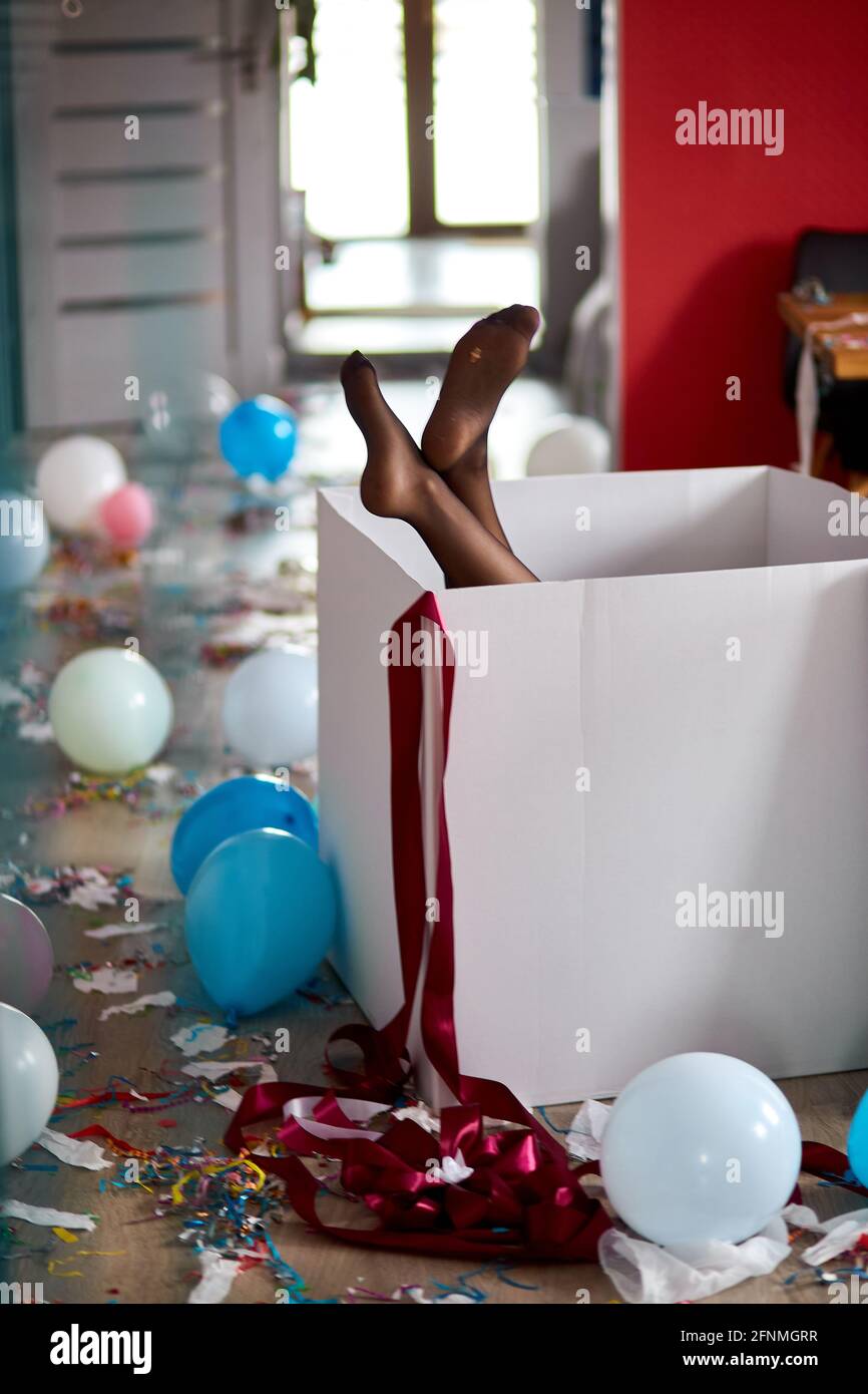 Frau Beine kleben aus großen Box mit undichten Strümpfen, nach Party Chaos, chaotisch im Wohnzimmer zu Hause, Konfetti und Ballons, Morgen nach Party cel Stockfoto