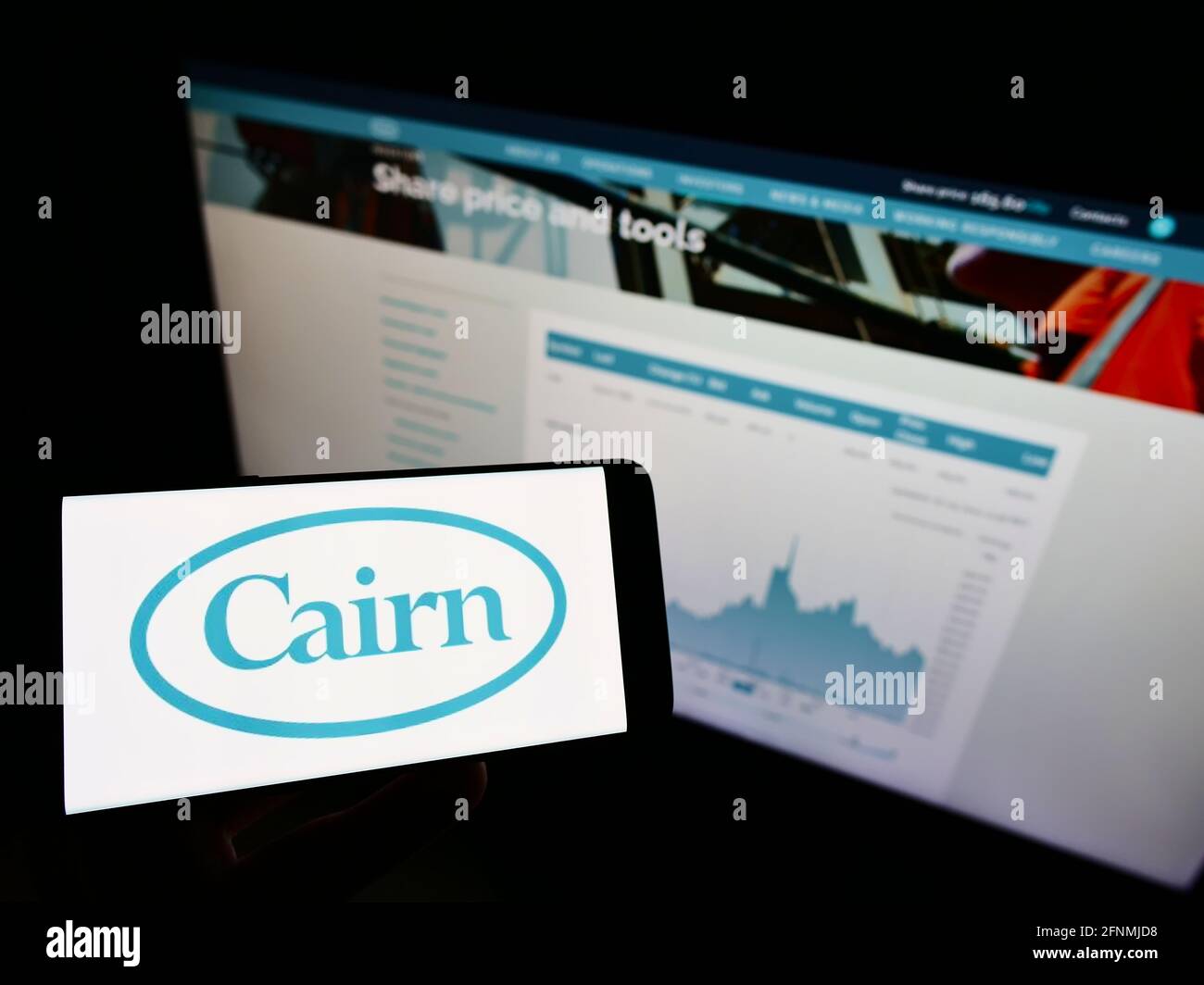 Person mit Mobiltelefon und Logo des britischen Öl- und Gasunternehmens Cairn Energy plc auf dem Bildschirm vor der Webseite mit Aktientabelle. Konzentrieren Sie sich auf die Telefonanzeige. Stockfoto