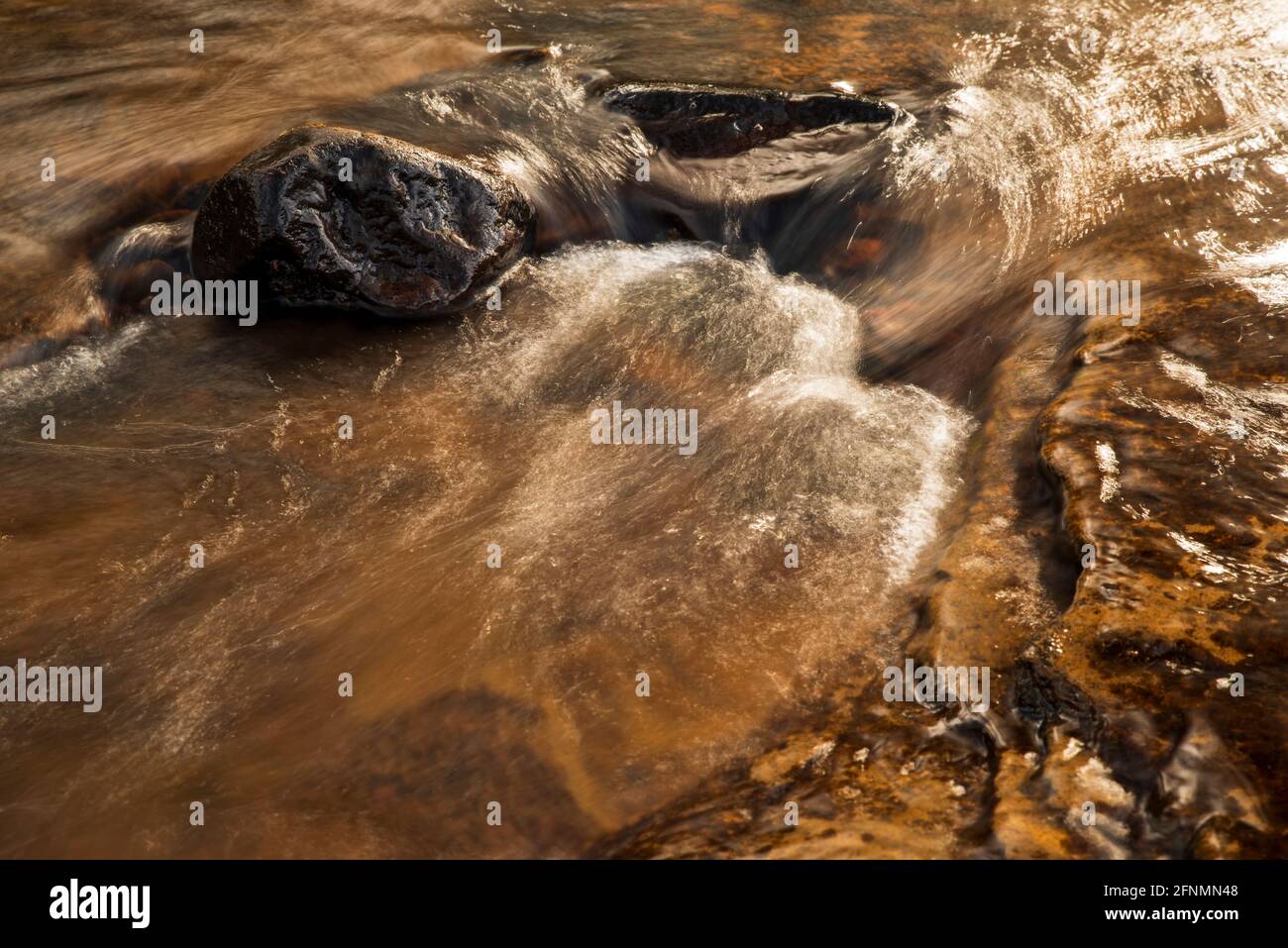 Das Sonnenlicht reflektiert sich von einer kleinen Kaskade auf dem Burn Anne Water in der Nähe von Galston in East Ayrshire, Schottland. Stockfoto