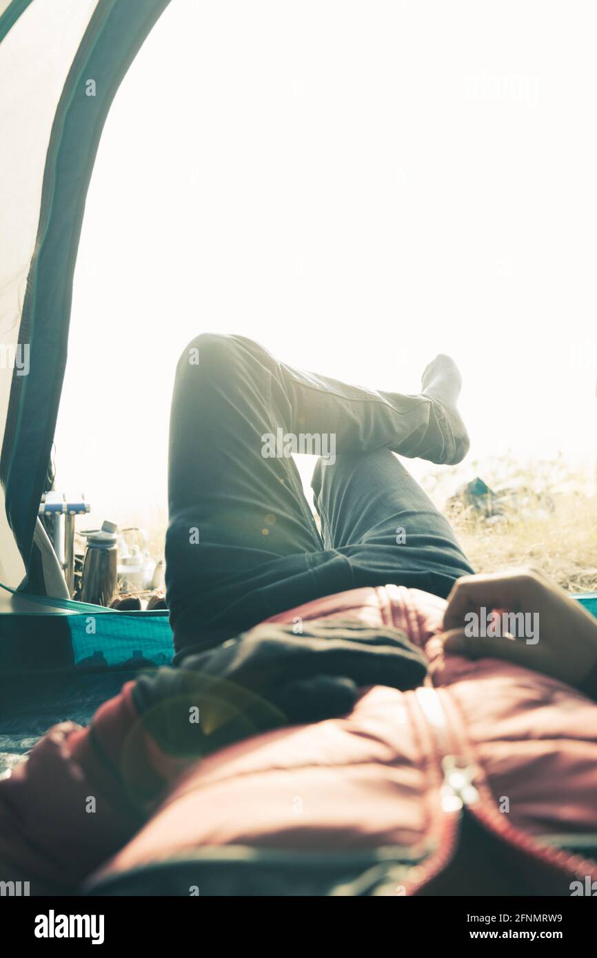 POV-Aufnahme eines Reisenden im Zelt, der sich während des nebligen Morgensonnenaufgangs auf dem Berg ausruhte - Konzept der Alleinreise während des Wanderns Stockfoto