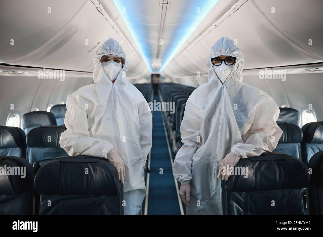 Zwei Mitarbeiter der Kabinencrew in Schutzüberalls in der Flugzeugkabine Stockfoto