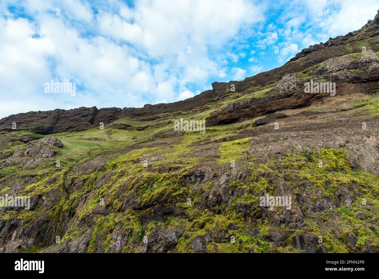 Blick auf eine steile, grasbewachsene Klippe unter blauem Himmel mit Wolken. Natürlicher Hintergrund. Stockfoto