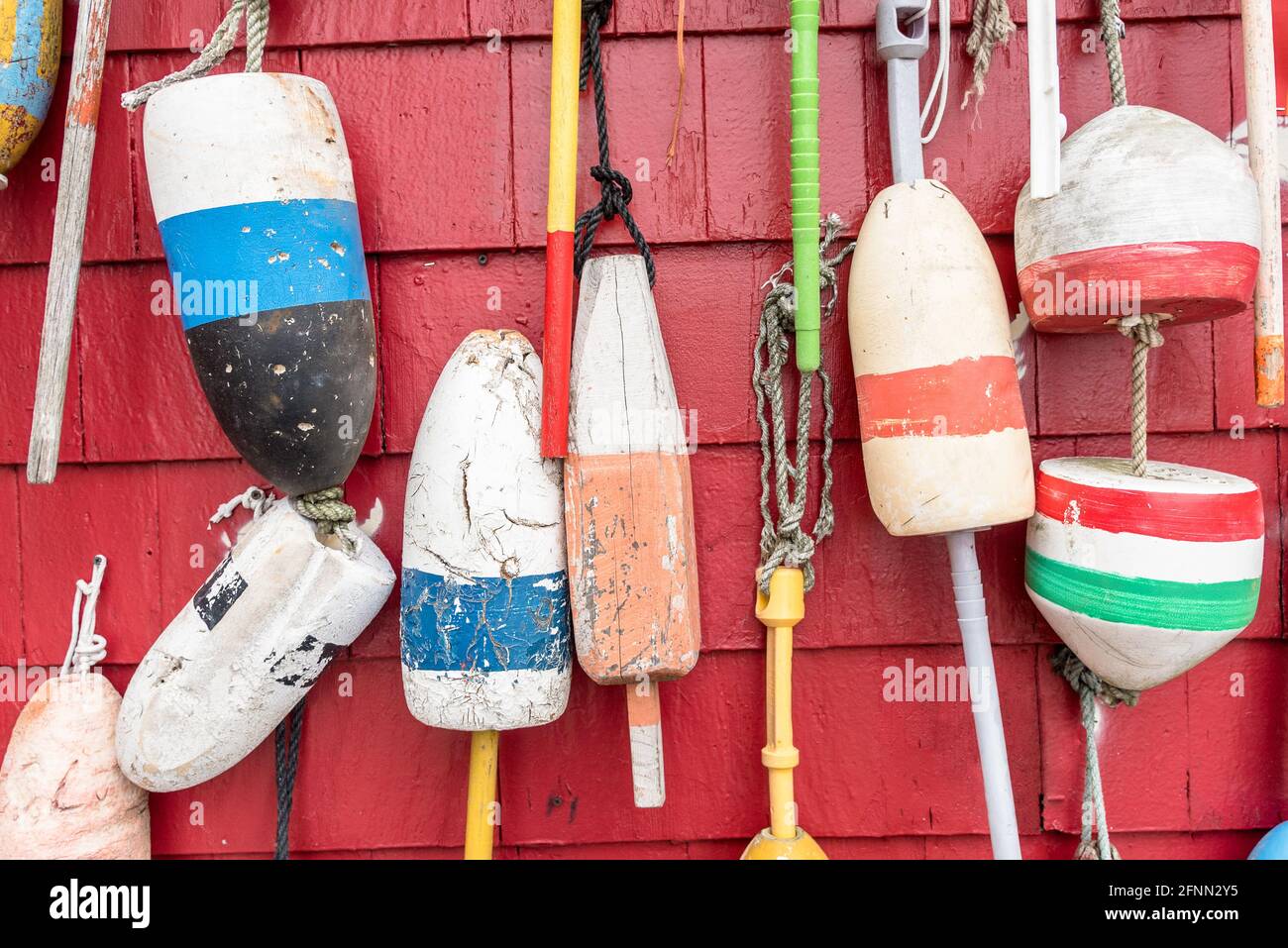 Nahaufnahme von bunten alten Fischerbojen, die auf dem hängen Externe rote Holzwand einer Fischerhütte in einem Hafen Stockfoto