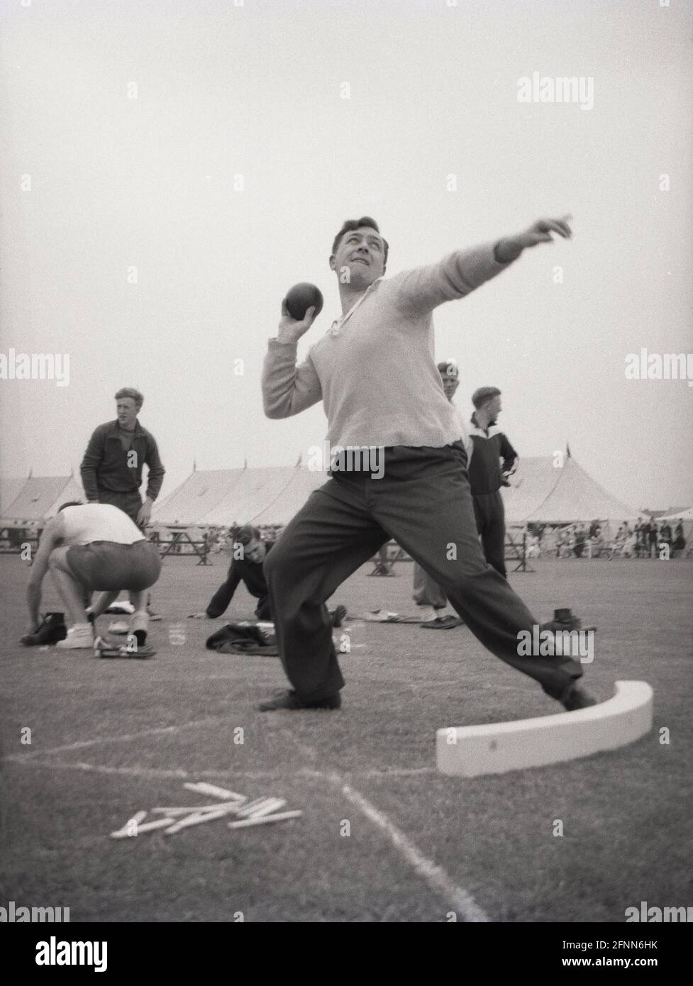 1954, historisch, ein Mann, der eine Hose, ein Hemd und einen Pullover  trägt und den Shotput wirft, bei einem Sporttag im öffentlichen Dienst,  England, Großbritannien, einem Amateursportereignis. Putting the Shot - ein