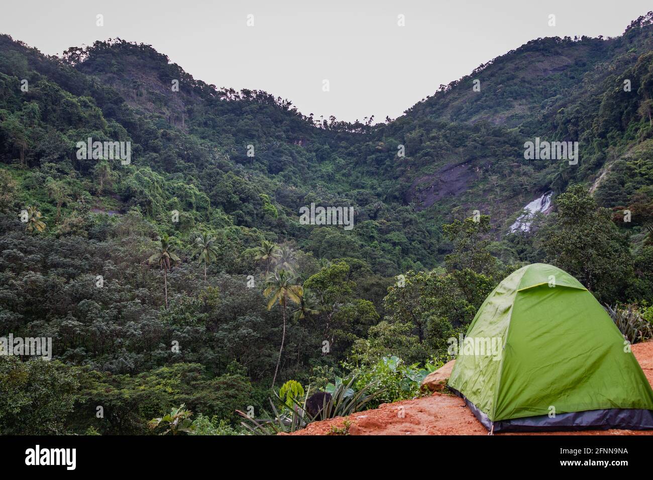 In diesem Bild wird das Camping-Erlebnis des Alleinreisenden mit seinem Fahrrad und seinem Zelt zum Ausdruck gebracht. Im Hintergrund sind Hügel, Wasserfall und grüne Wälder zu sehen. Stockfoto