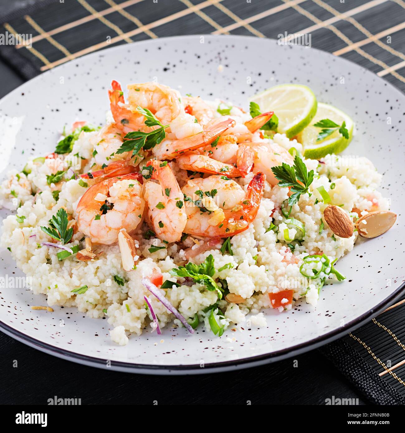 Couscous mit gerösteten Garnelen, Tomaten, roten Zwiebeln, Mandelnüssen und Petersilie. Marokkanisches Essen mit Couscous und Garnelen. Stockfoto
