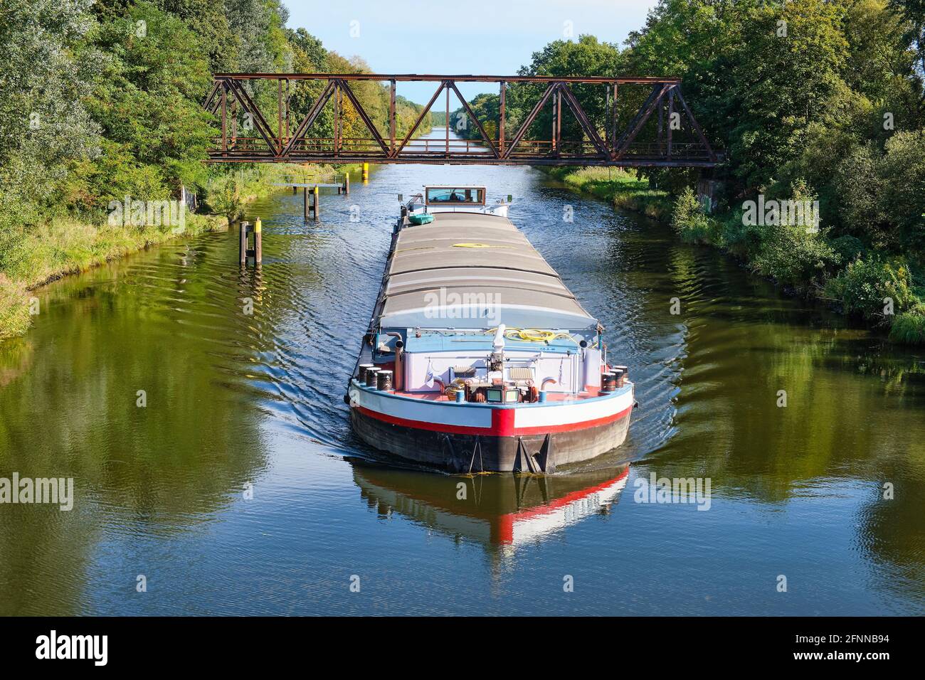 Das Frachtschiff passiert an einem sonnigen Herbsttag unter einer alten Eisenbrücke. Reflexionen im Wasser Stockfoto