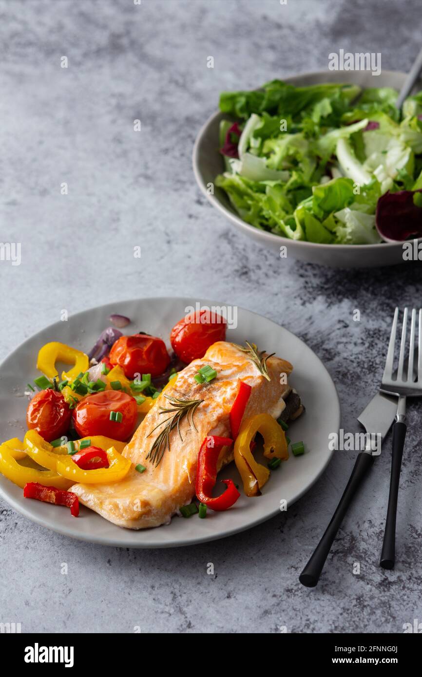 Gebackenes rotes Fischfilet Arctic Saibling auf einem Teller mit Gemüse, Salat in einer Schüssel mischen, leckeres herzhaftes gesundes Abendessen Stockfoto