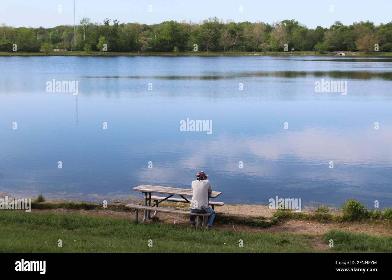 Mann, der an einem Picknicktisch am Axhead Lake in des Plaines, Illinois, mit einer schönen Reflexion sitzt Stockfoto