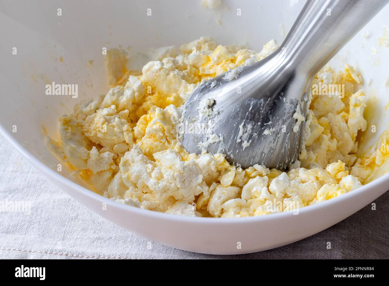 Teig in einer weißen Schüssel mit einem Stabmixer mischen. Zutaten - Quark, Butter, Ei und Zucker. Der Prozess der Herstellung von Quark Bagels oder Crois Stockfoto