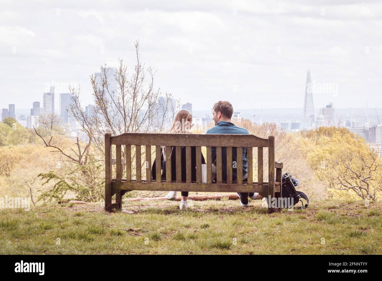 Ein Paar (männlich und weiblich), das während der Coronavirus-Pandemie in Großbritannien auf einer Bank auf Hampstead Heath mit Blick auf die City of London sitzt Stockfoto