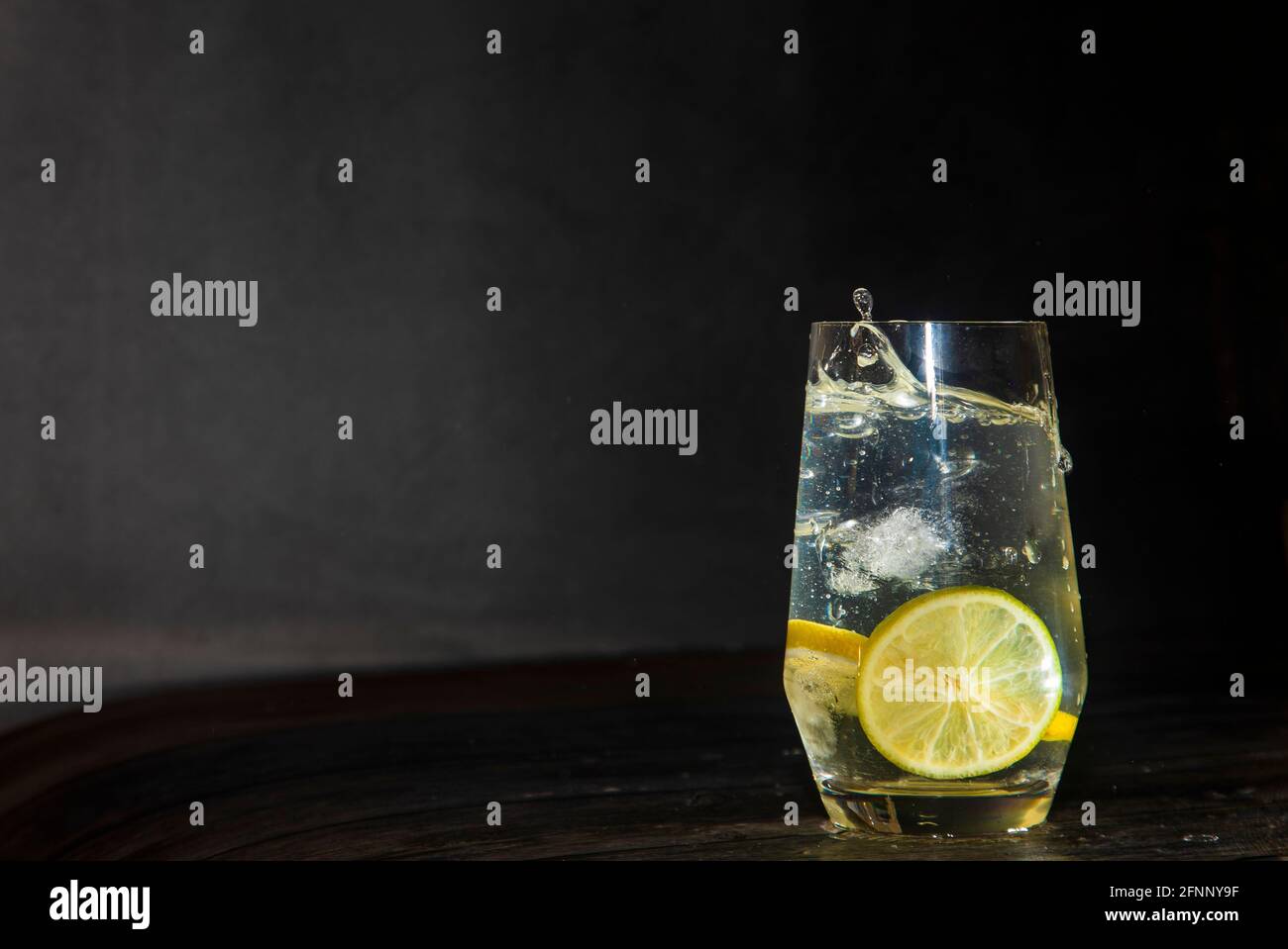 Eiswürfel in ein Glas Wasser mit Limette, Zitrone und Eiswürfeln geben Stockfoto