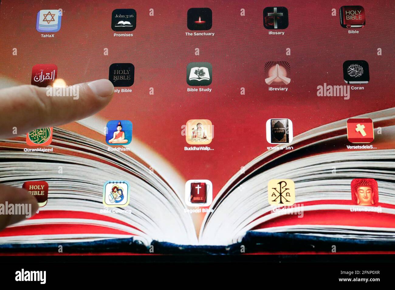 Mann liest ein digitales Tablet iPad mit verschiedenen religiösen digitalen Apps. Christentum, Islam, Judentum, Buddhismus. Interreligiöse Symbole. Frankreich. Stockfoto