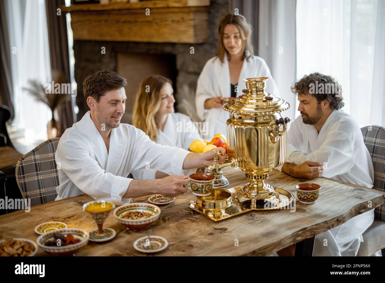 Gesellschaft der erwachsenen Freunde im Bademantel, die auf dem gedienten Tisch im russischen Stil mit samowar im Badehaus sitzen. Entspannen und gemeinsam im Spa genießen. Wellness und Freizeit. Stockfoto