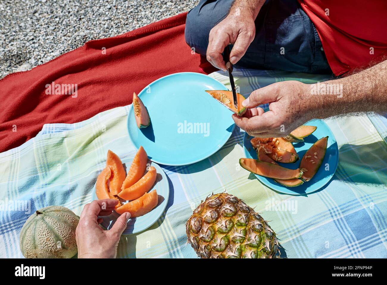 Ehepaar mittleren Alters bei einem Picknick am Meer mit frischen exotischen Früchten. Mann schneidet eine Melone. Frühling, Sommer Lifestyle, Liebe Dating-Konzept. Stockfoto