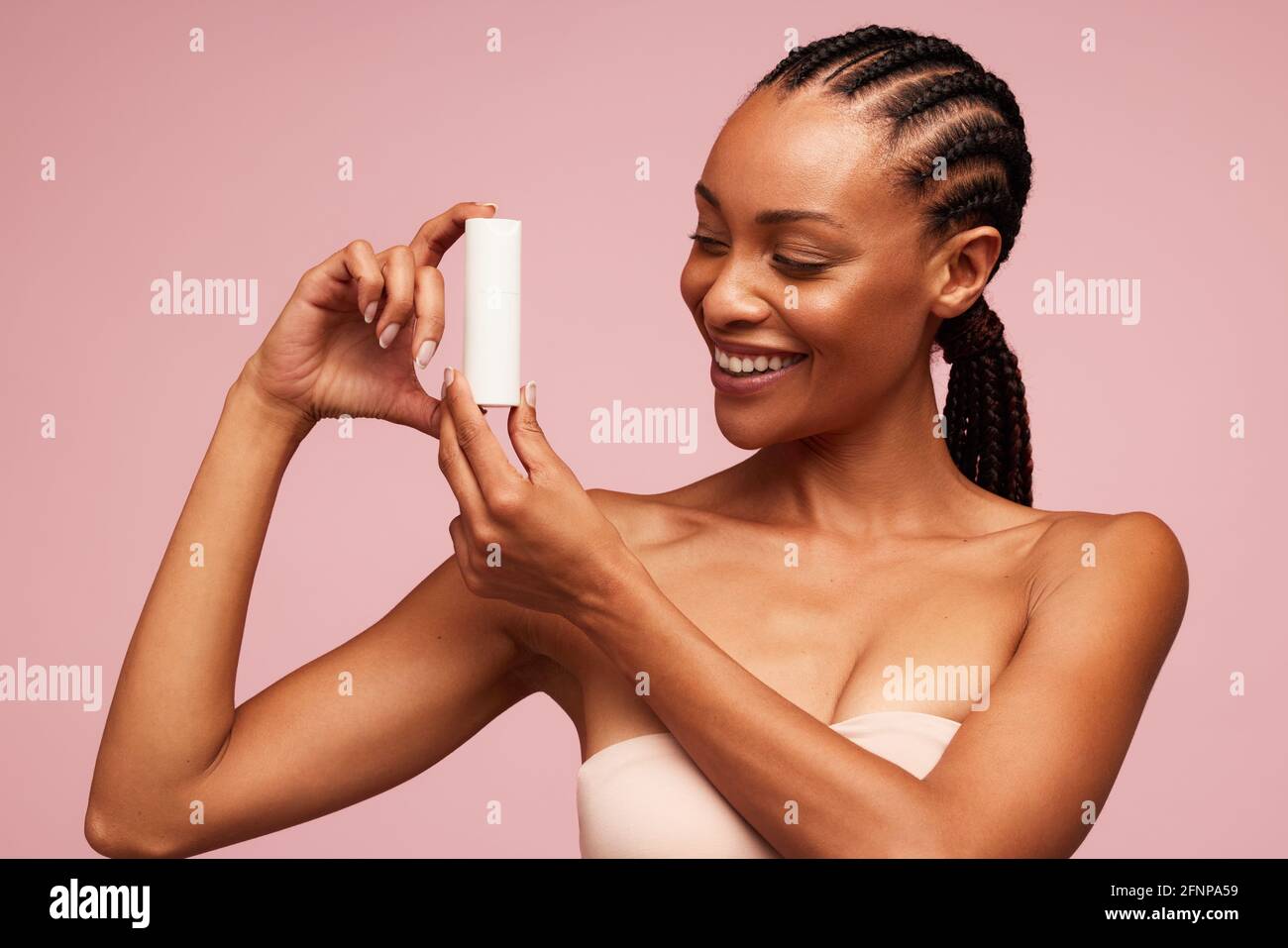 Glückliche afrikanische Frau mit einem kosmetischen Produkt. Weibliches Modell mit schöner Haut, die ein Hautpflegeprodukt zeigt. Stockfoto