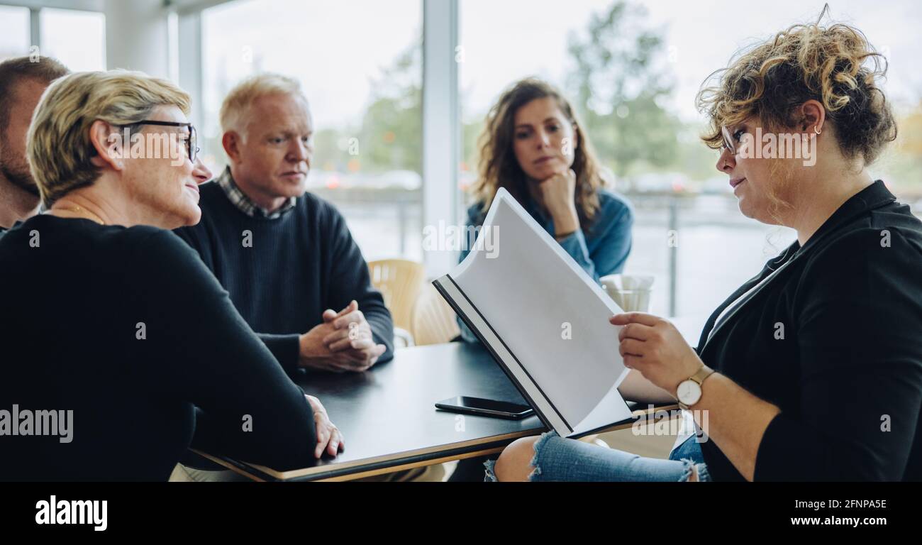 Geschäftsfrau liest ein Vertragsdokument mit Kollegen, die am Tisch sitzen. Geschäftsteam diskutiert eine Vereinbarung in einem Meeting. Stockfoto