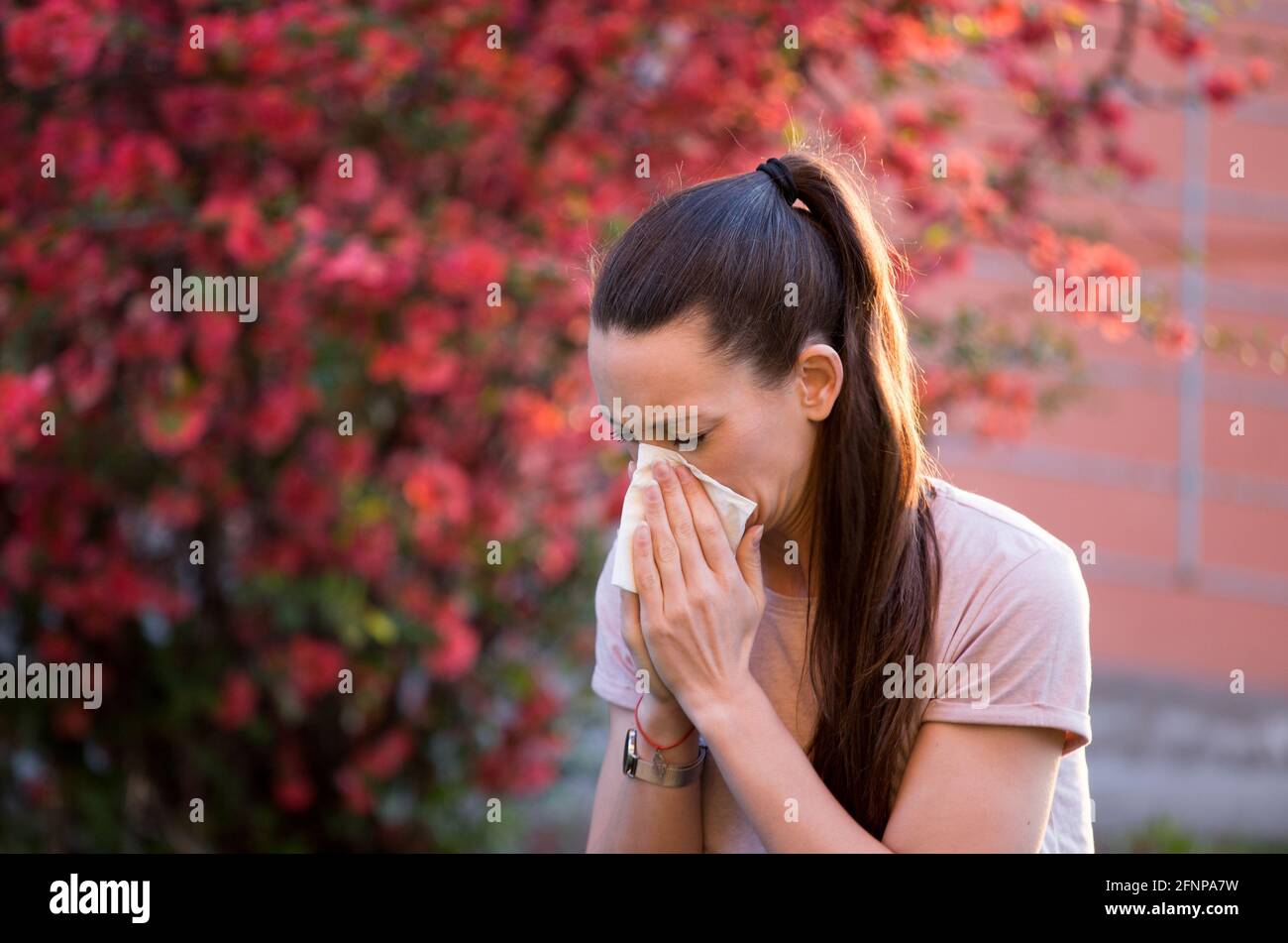 Junge hübsche Frau niest vor blühendem Baum. Frühjahrsallergiekonzept Stockfoto