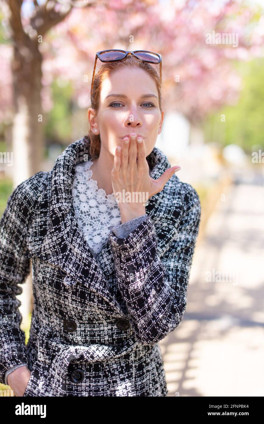 Glückliche junge Frau sendet Kuss im Park im Frühling während Sakura, Kirschbaum blüht Stockfoto