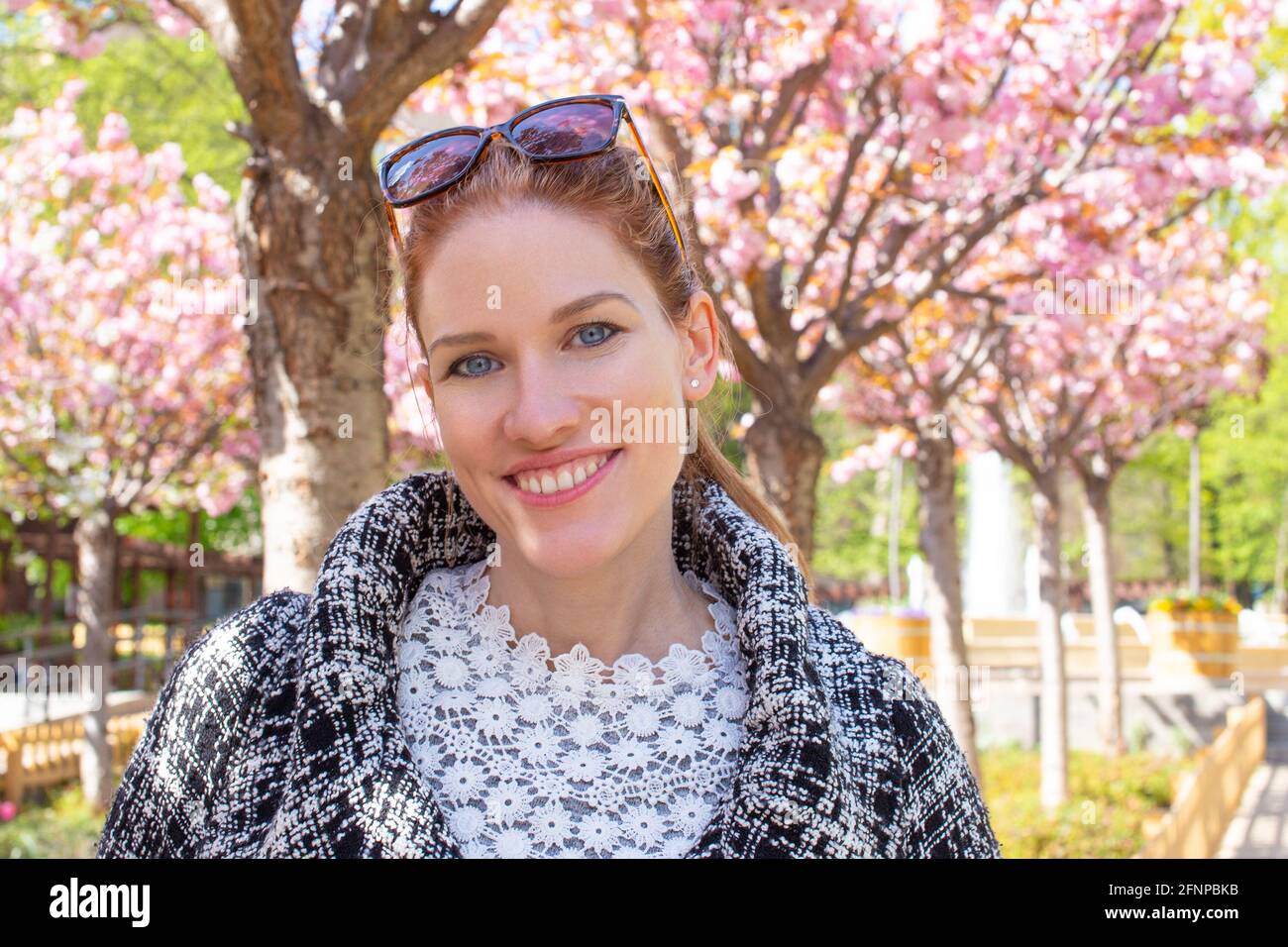 Glückliche junge kaukasische Frau im Park toothy Lächeln während Sakura Porträt, Kirschblütenbaum Stockfoto