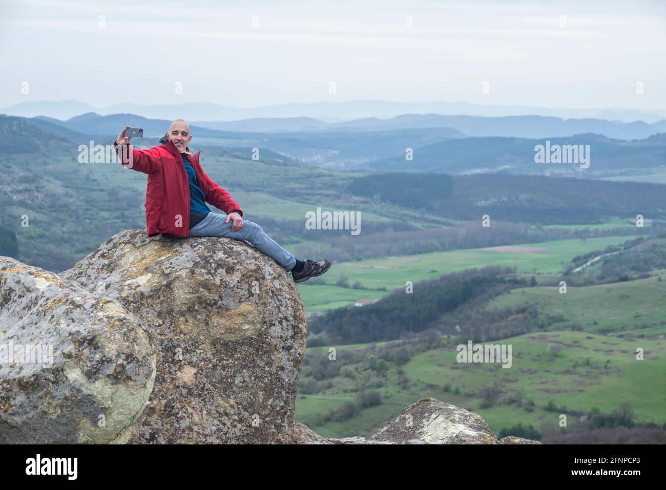 Perperikon, Bulgarien - April 24 2021: Ein Mann sitzt auf einem Felsen und macht ein Selfie Stockfoto