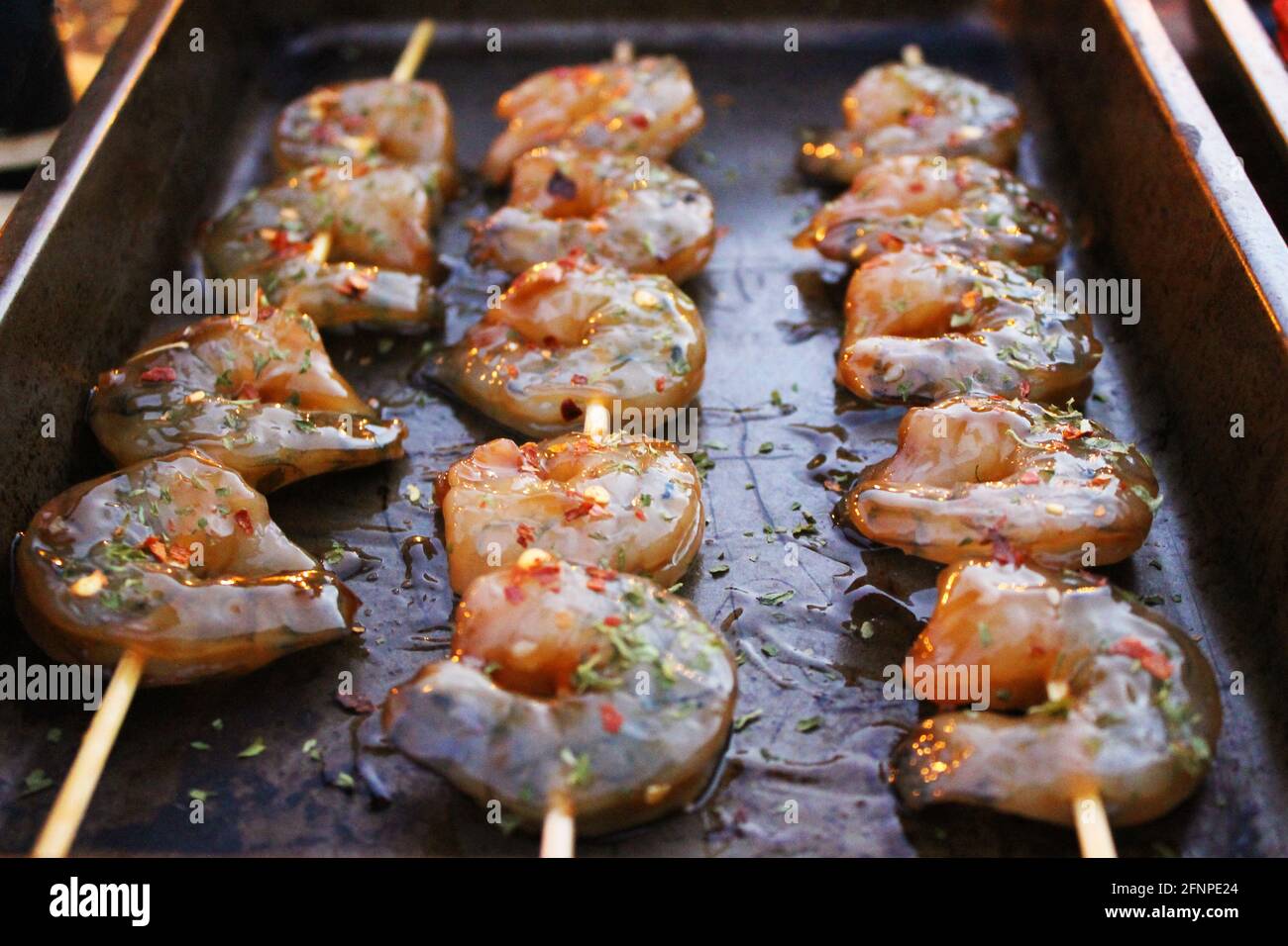Nahaufnahme von gewürzten und marinierten Garnelen auf Spiessen, in einer Pfanne mit Olivenöl. Stockfoto