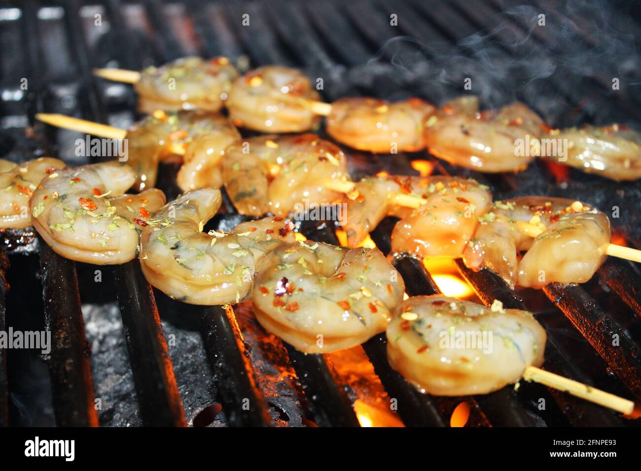 Nahaufnahme von glasierten und erfahrenen Garnelen auf Spiessen, die auf einem Grill gegrillt werden. Stockfoto