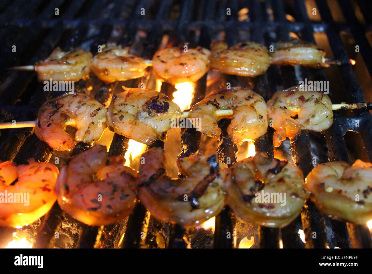 Nahaufnahme von glasierten und erfahrenen Garnelen auf Spiessen, die auf einem Grill gegrillt werden. Stockfoto