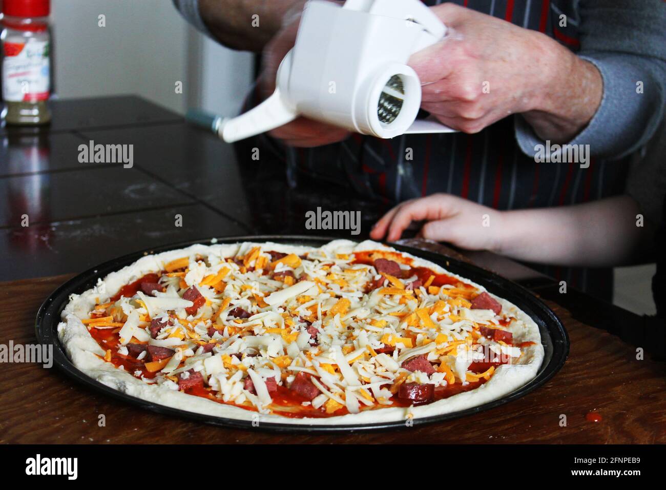 Nahaufnahme einer Frau und eines kleinen Kindes, die hausgemachte Pizza zubereiten. Hände nur im Rahmen. Stockfoto