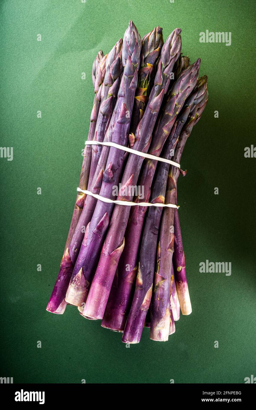 Frischer roher Bio-Spargelstrauß, violettes, grünes und weißes Gemüse auf dunkelgrünem Hintergrund Stockfoto