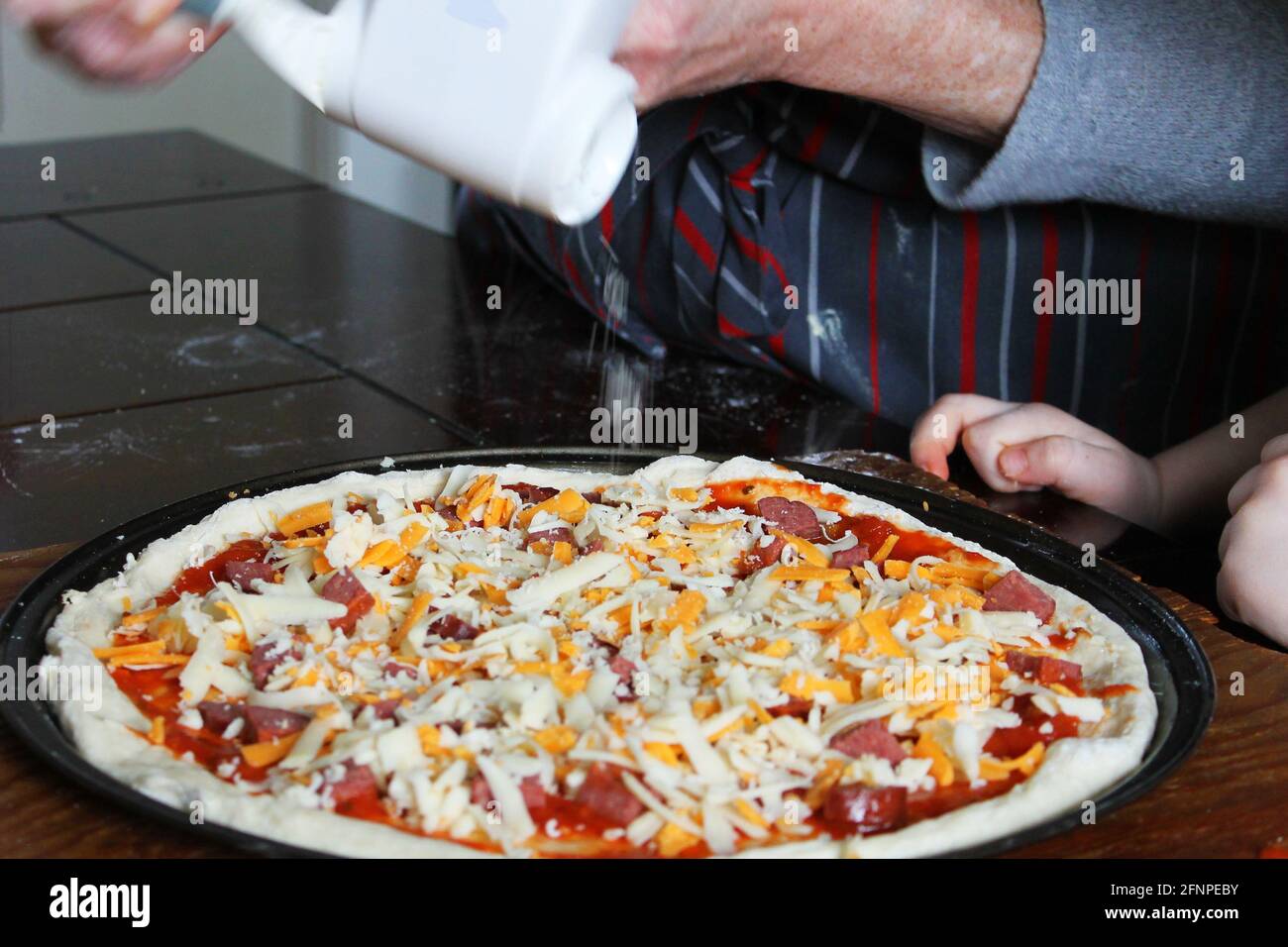 Nahaufnahme einer Frau und eines kleinen Kindes, die hausgemachte Pizza zubereiten. Hände nur im Rahmen. Stockfoto