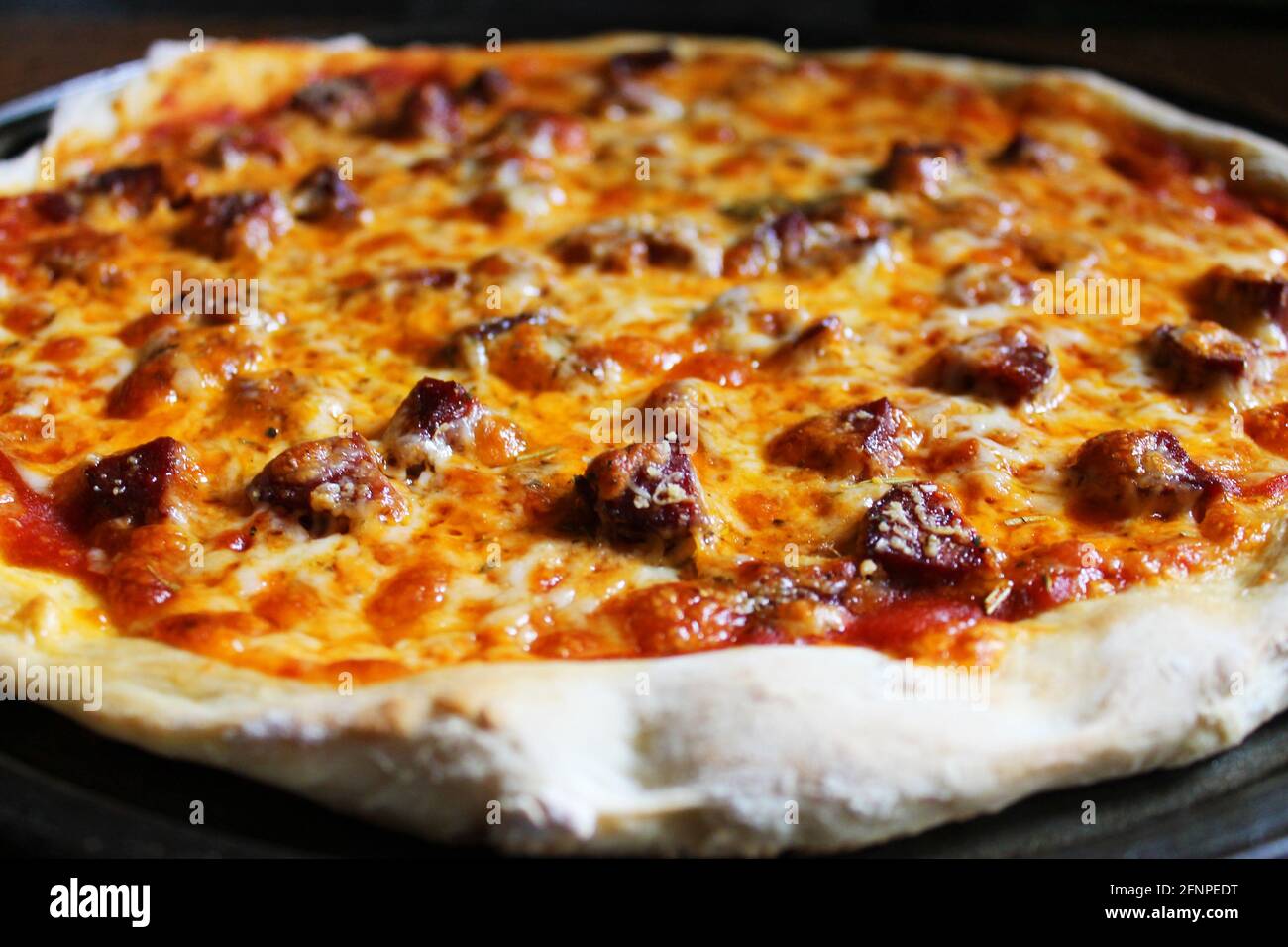 Nahaufnahme von frisch gebackener, hausgemachter Pizza, immer noch in der Pfanne, auf Holzschneidebrett. Stockfoto
