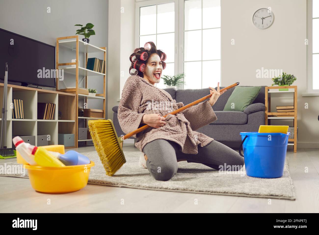 Lustige Hausfrau, die das Haus putzt, singt und spielt auf einem Besen, wie auf einer imaginären Gitarre. Stockfoto