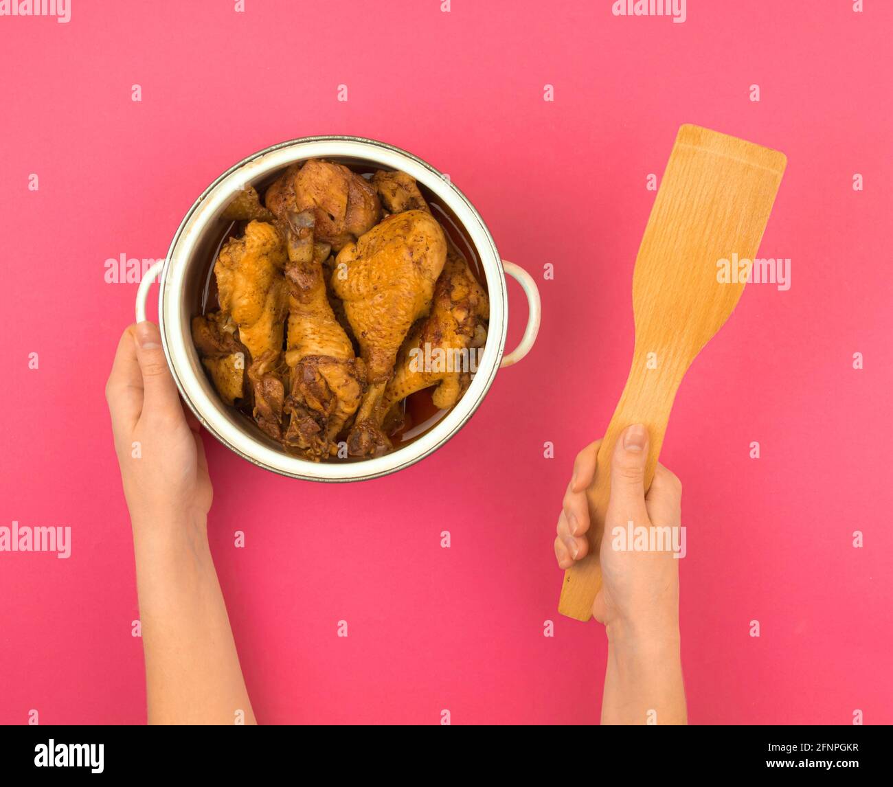 Frau mit einem Topf gefüllt mit gebratenem Huhn und mit einem Holzspatel, rosa flach Lay Hintergrund, Draufsicht Stockfoto