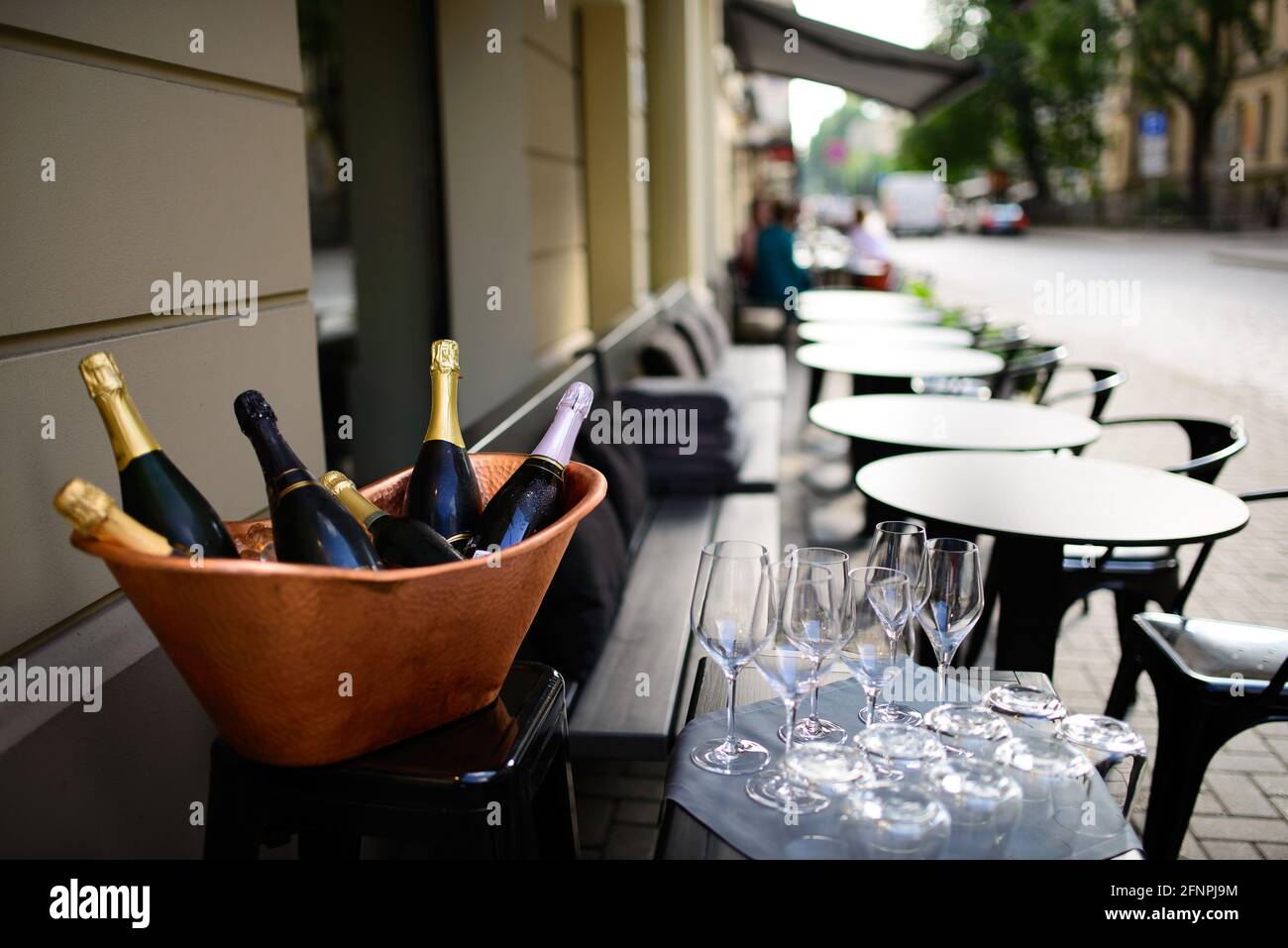 Flaschen Champagner und Sekt in Kupfereikübel Und Gläser in der Nähe mit einer Reihe von leeren Tischen und Stühlen Auf der Terrasse des Restaurants Stockfoto