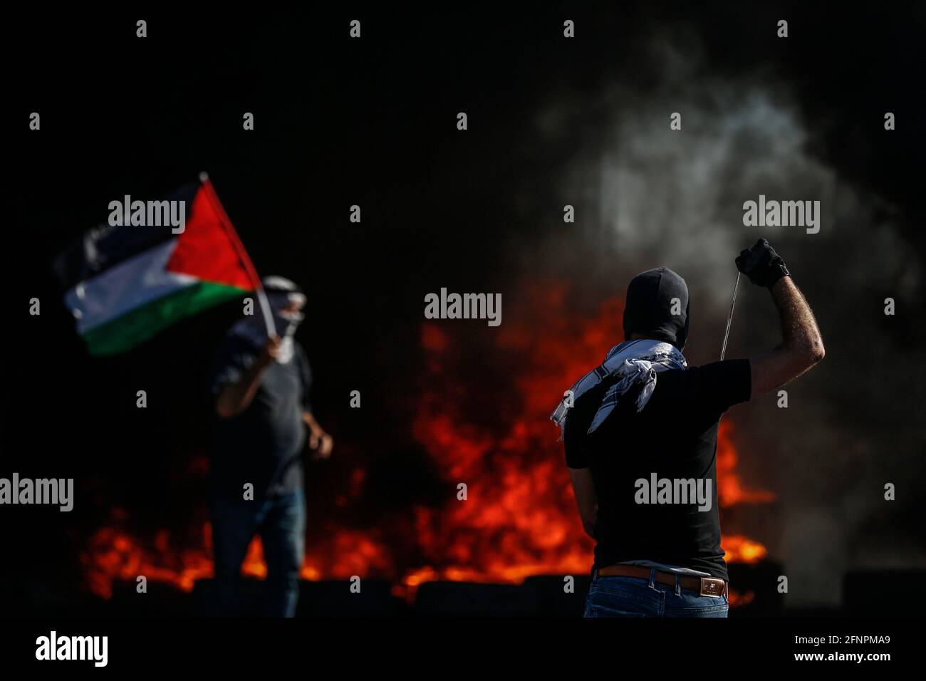 Nablus, Palästinensische Gebiete. Mai 2021. Ein palästinensischer Protestler bereitet eine Schleuder vor, um Steine auf israelische Sicherheitskräfte zu schleudern, während ein anderer die palästinensische Flagge während der Zusammenstöße am Checkpoint Huwwara hält, während die israelisch-palästinensische Gewalt eskaliert. Quelle: Ayman Nobani/dpa/Alamy Live News Stockfoto