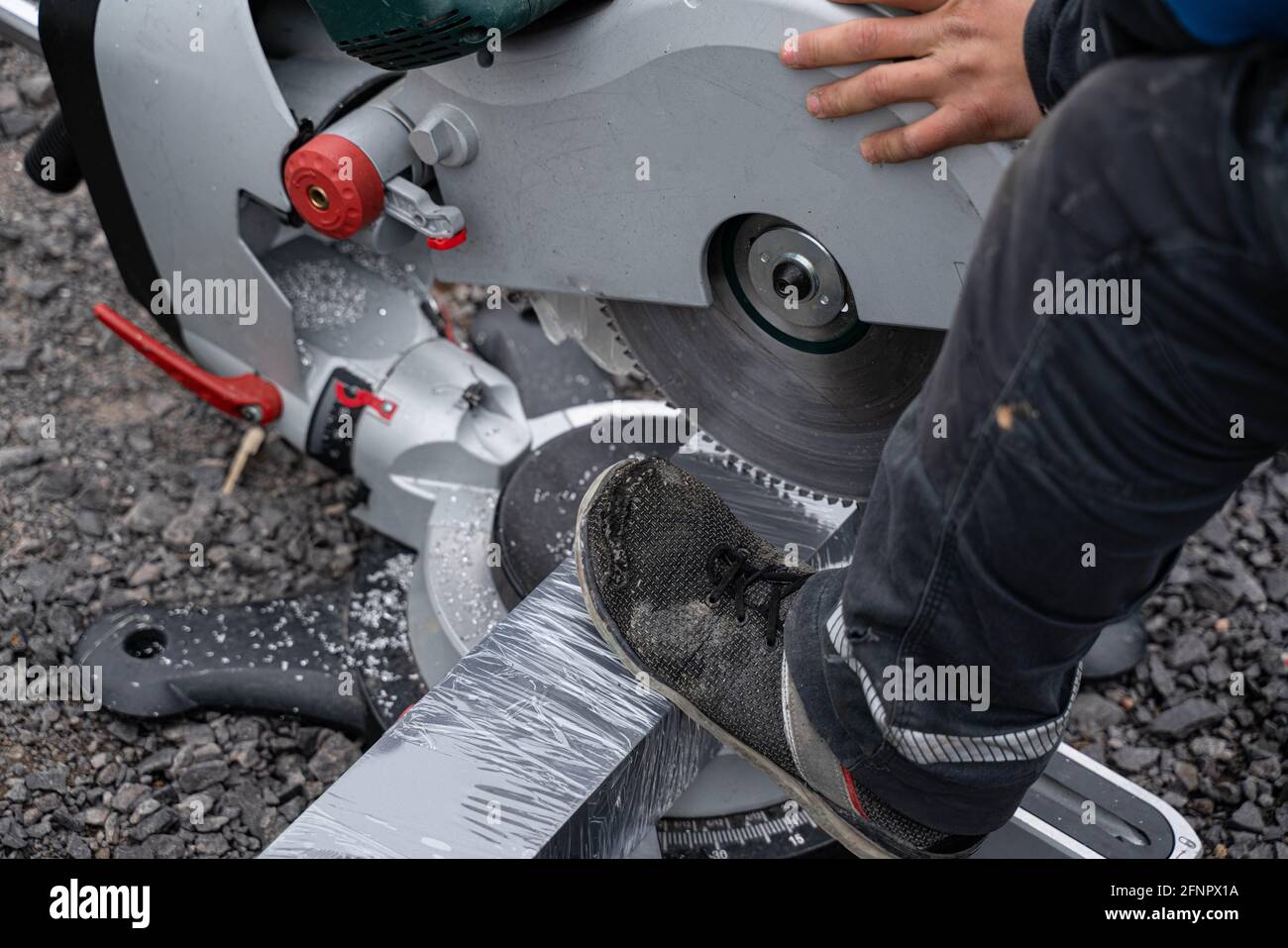 Mann schneidet großes Stück Aluminium mit elektrischer Kreissäge Stockfoto