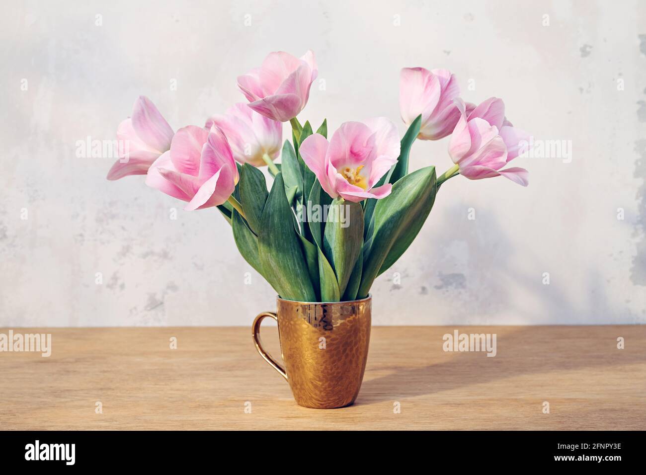 Rosafarbene Tulpen in einem goldenen Becher auf einem Holztisch Stockfoto