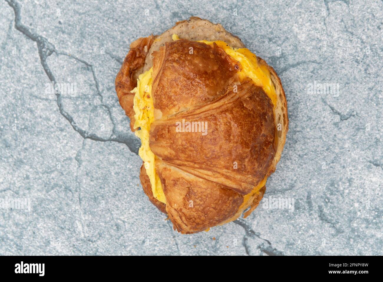 Blick von oben auf ein köstliches Croissant-Sandwich mit Rührei, geschmolzenem Käse und Würstchen für eine komplette Mahlzeit. Stockfoto