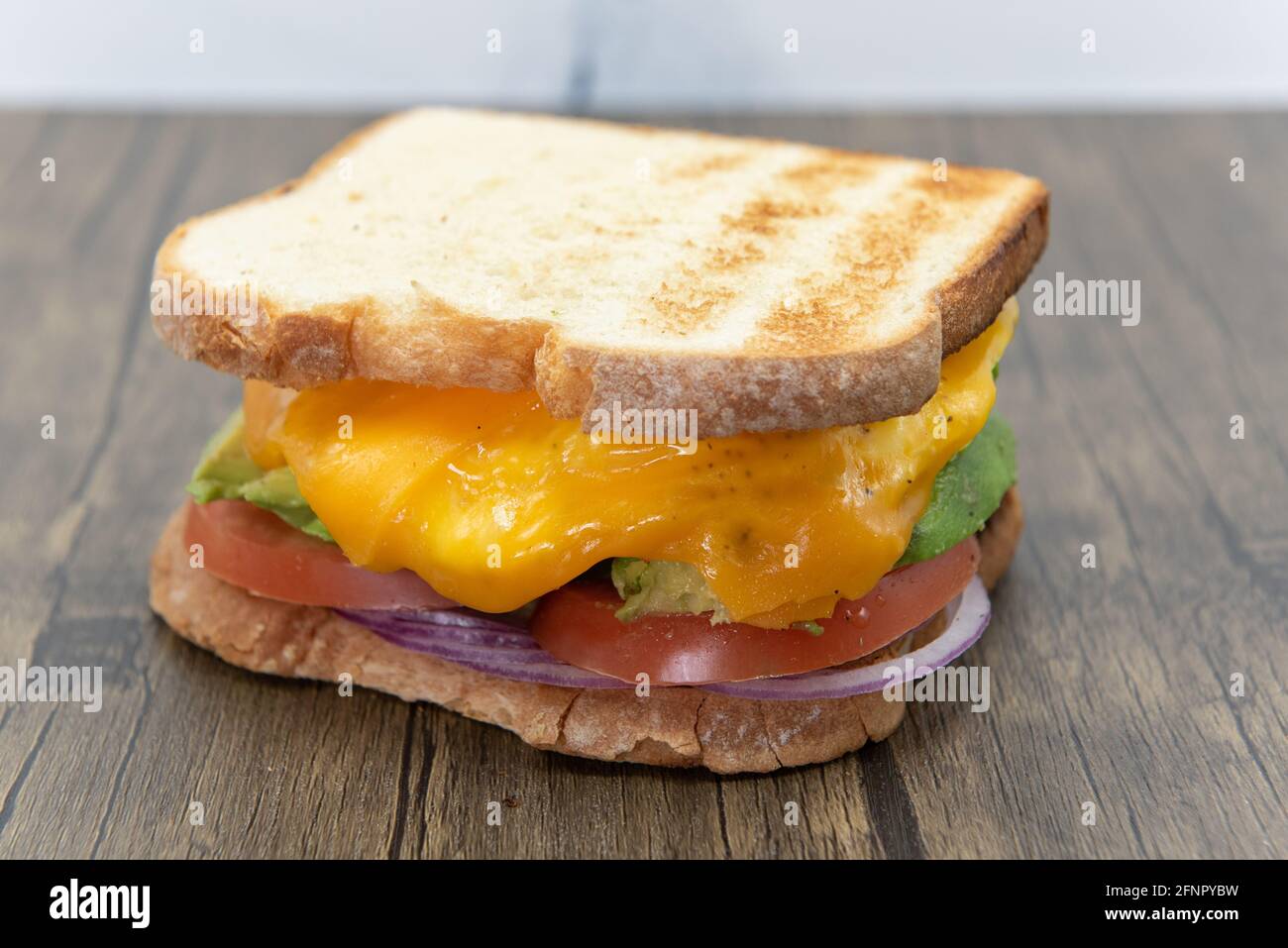 Geröstetes Brot an beiden Enden dieses dicken Ei- und Avocado-Sandwiches mit Avocado, geschmolzenem Käse, Zwiebeln und Tomaten. Stockfoto