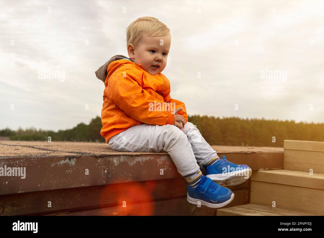 Kleiner Junge in orangefarbener Jacke sitzt auf einer Holztreppe Stockfoto