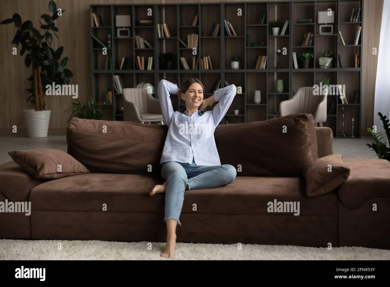 Ruhige junge Dame sitzt in entspannter Haltung auf dem bequemen Sofa Stockfoto