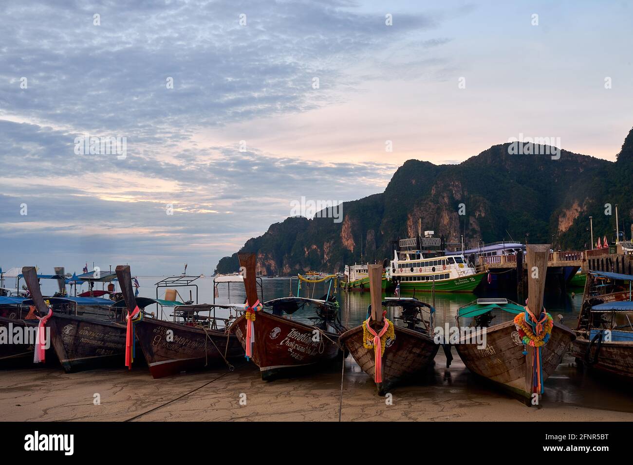 Bei Ebbe auf der Tonsai Bay in der Morgendämmerung, Kho Phi Phi, Thailand, verankerte Longtail-Boote mit gefesselten Stücken farbigen Seidentuchs auf ihren Bögen Stockfoto