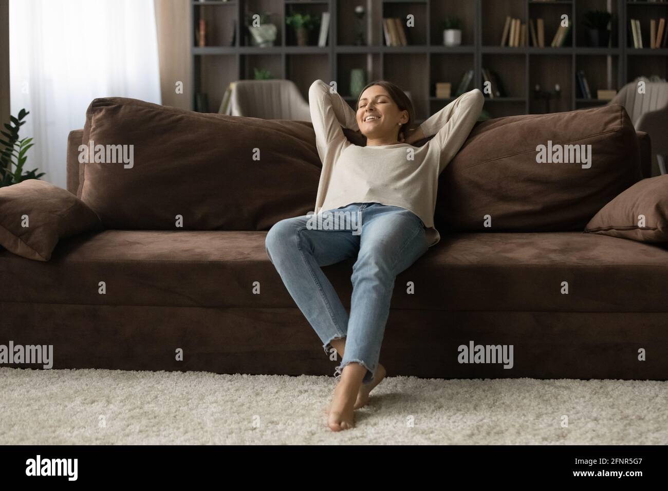 Friedliche Teenager-Frau, die sich auf einem gemütlichen Sofa in einer modernen Wohnung zurücklehnen kann Stockfoto