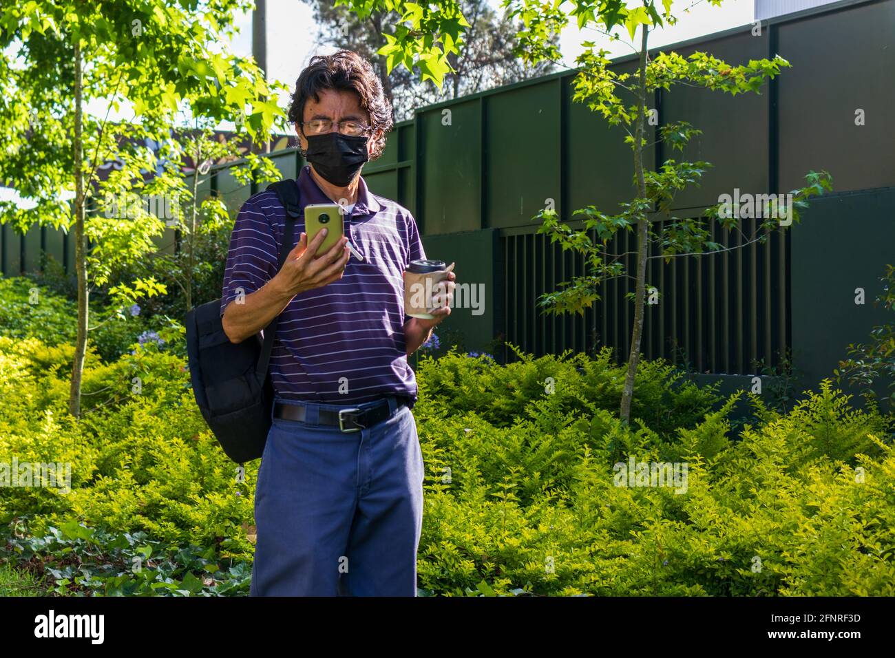 Hispanic Mann trägt eine Gesichtsmaske auf einem Park trinken Kaffee Stockfoto