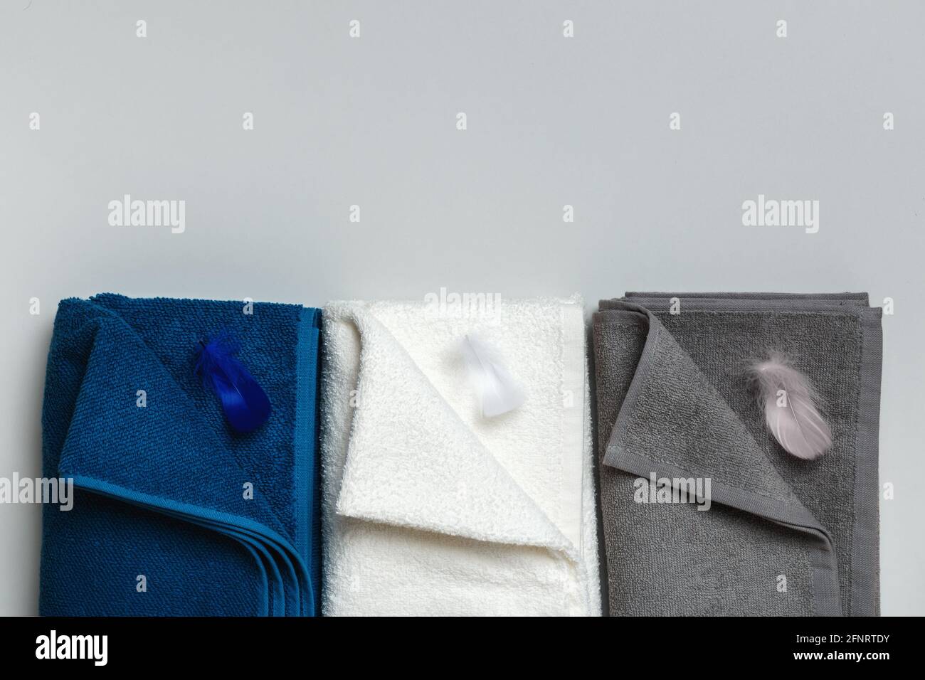 Drei Frottee Handtücher in blau, weiß und grau mit Federn. Flache, layierte Draufsicht mit Platz für Text. Stockfoto