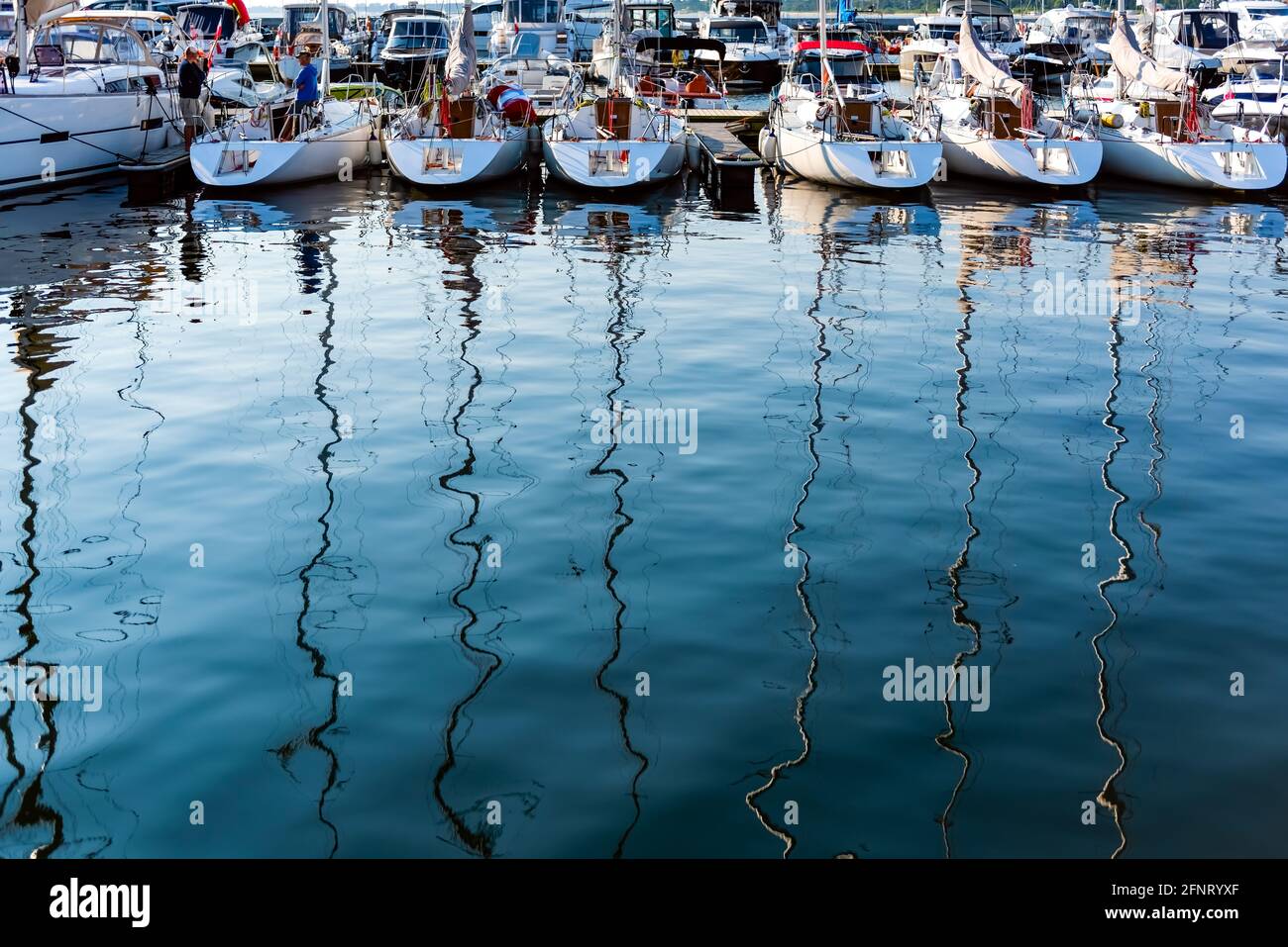 Segelyachten liegen an einem Pier in einem Hafen an der ostsee an einem sonnigen Morgen, Blick auf die hinteren Decks und Reflexion im Wasser. Nautisches Schiff für Cha Stockfoto