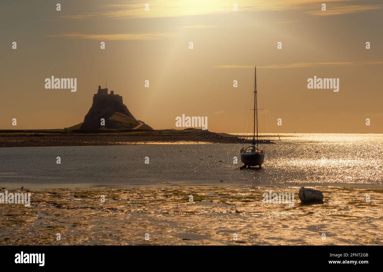 Lindisfarne, vor der Nordostküste Englands auch als Heilige Insel bekannt. Sonnenstrahlen erhellen den Hafen mit dem ikonischen Schloss im Hintergrund Stockfoto