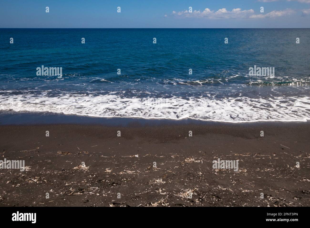 Einzigartige schwarze Sandstrände von Santorini, Griechenland, aufgenommen an einem sonnigen Tag mit den Wellen, die hereinbrechen. Stockfoto